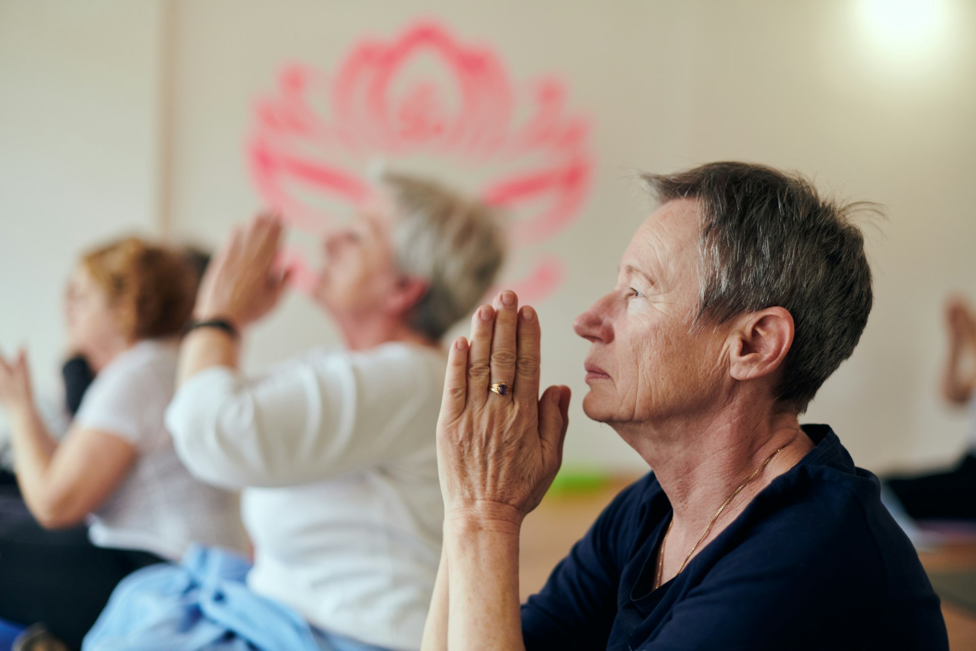 A group of senior women engage in various yoga exercises, including neck, back, and leg stretches