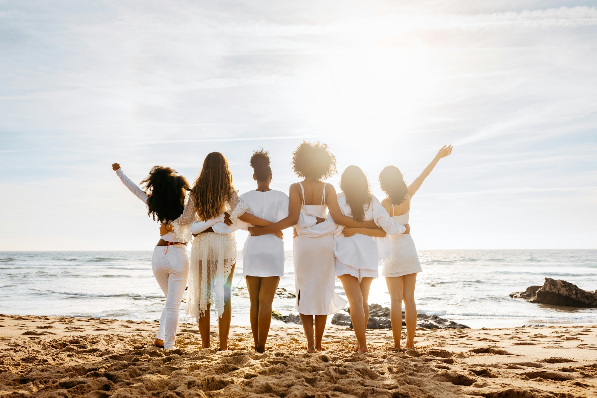 Bride's team. Back view of group of young diverse women posing and embracing by the seashore. Hen