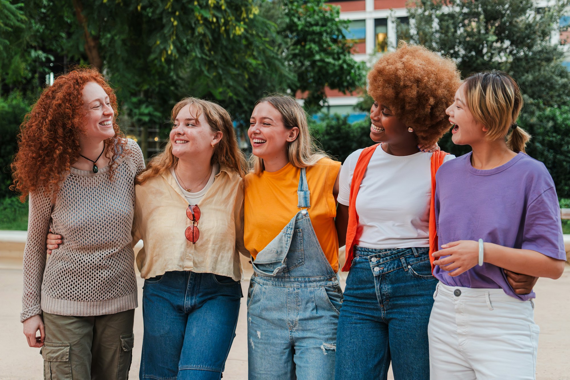 Group of joyful young women, laughing and enjoying a weekend trip. Real cool girls walking embracing
